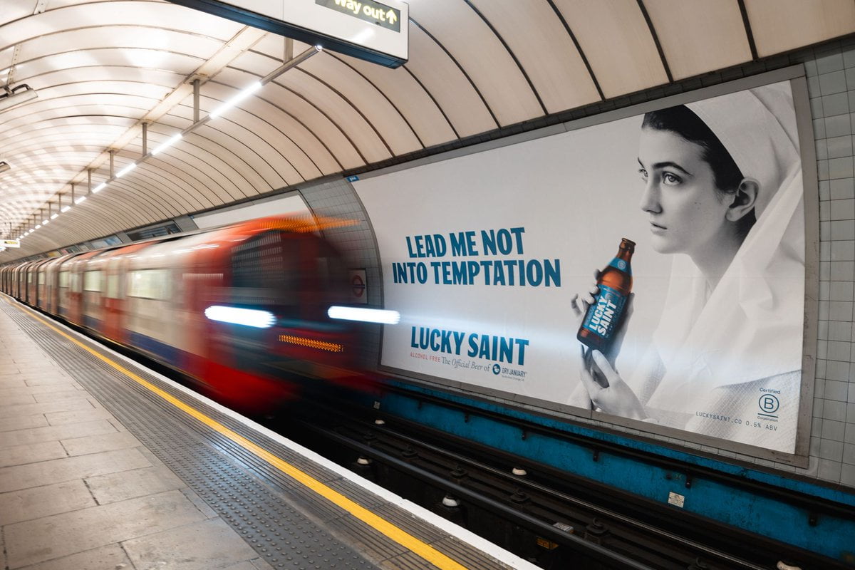 A beer advert for Lucky Saint non-alcoholic beer brand. Across the track on the London Underground with a train approaching.