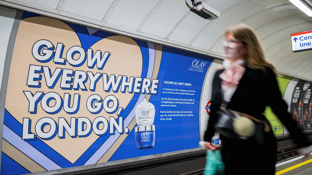 A woman walking past a cross-track 48 sheet advert on the London Underground, displaying an Olay advert.