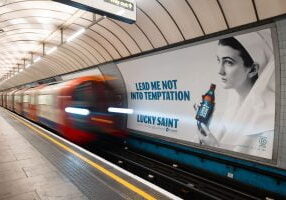 A beer advert for Lucky Saint non-alcoholic beer brand. Across the track on the London Underground with a train approaching.