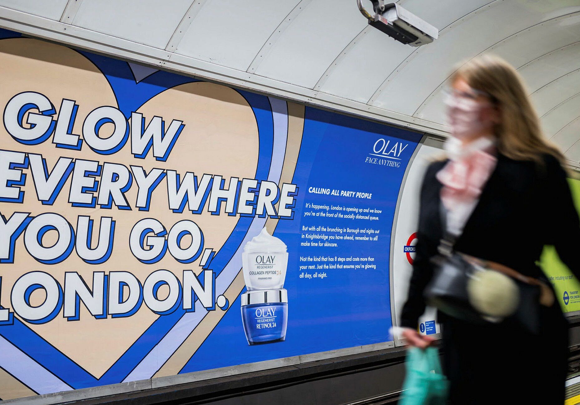 A woman walking past a cross-track 48 sheet advert on the London Underground, displaying an Olay advert.
